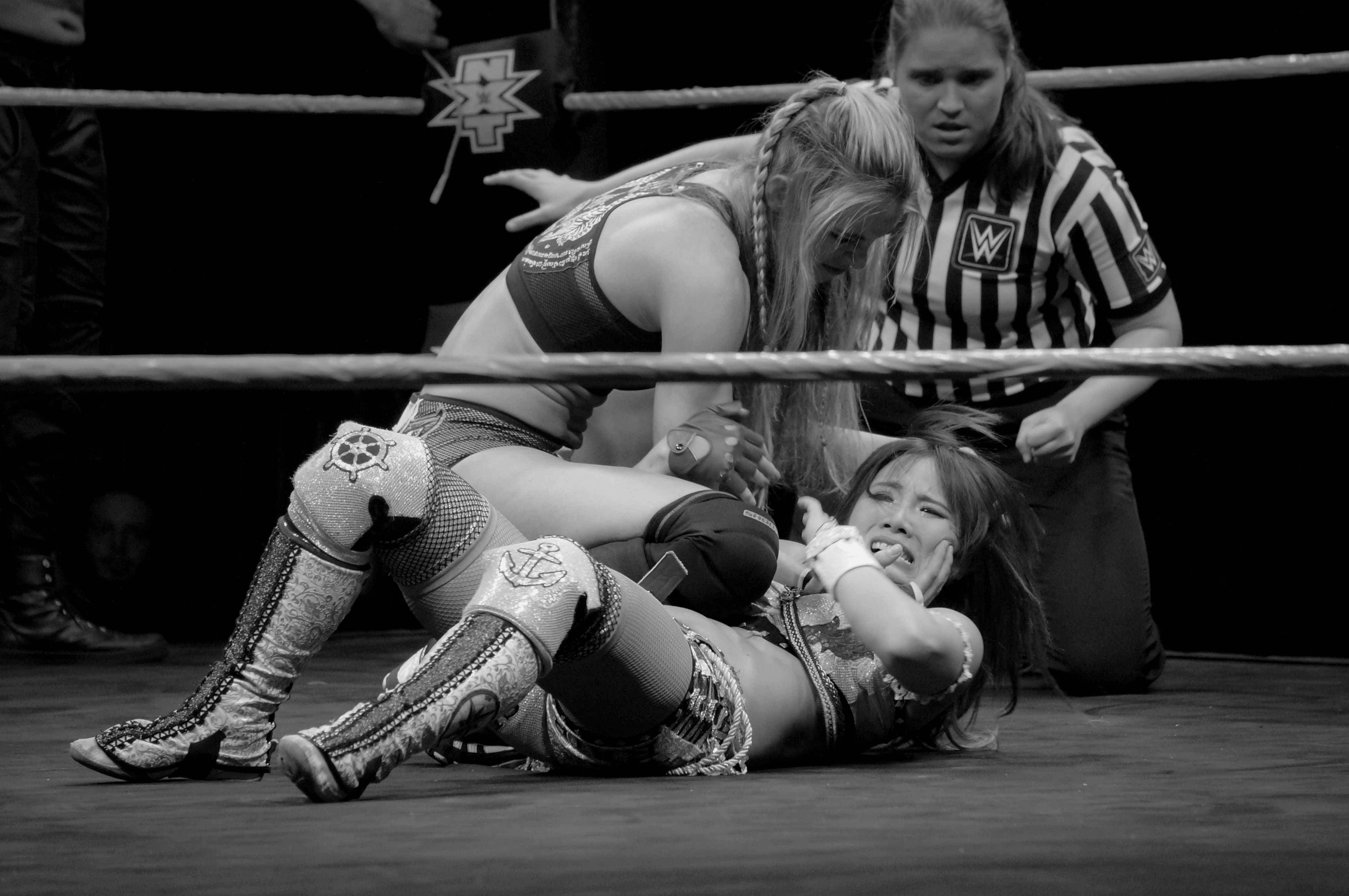 Two women wrestling with ref overlooking